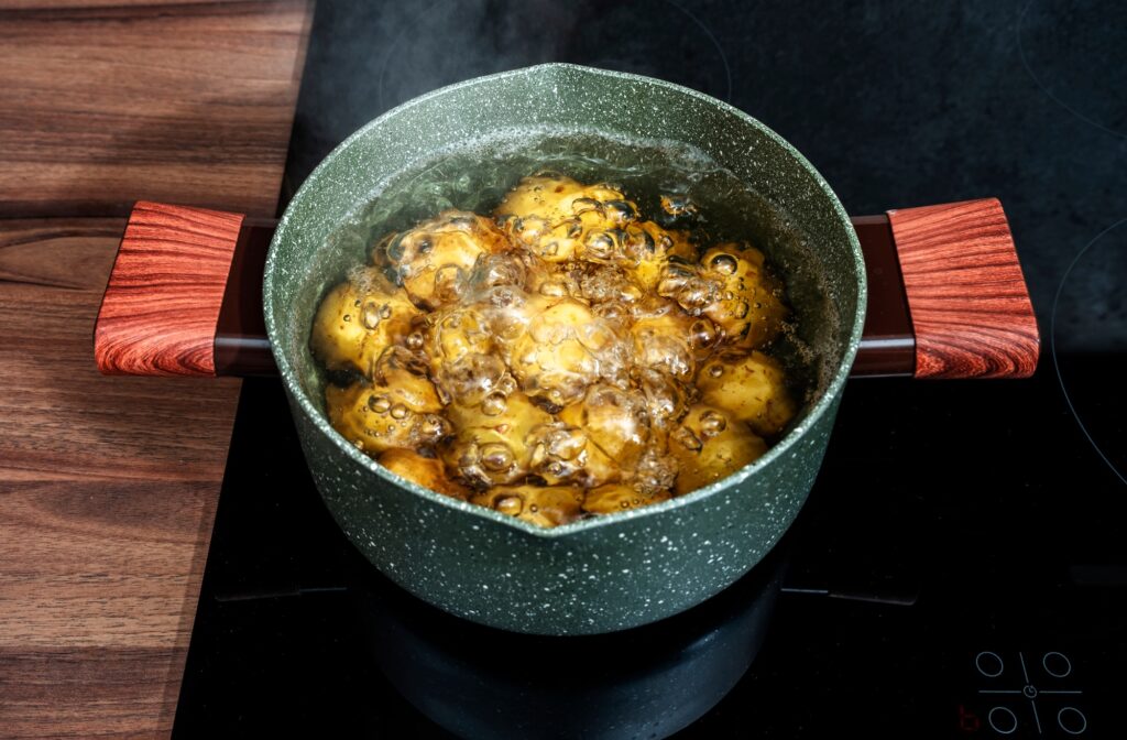 Baby potatoes in green pot boiling and steaming in water on induction hob