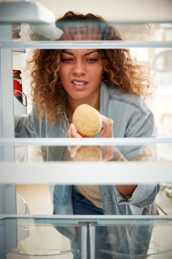 Disappointed Woman Looking Inside Refrigerator Empty Except For Potato On Shelf